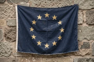 Drapeau européen aux douze étoiles dorées accroché sur un mur en pierre ancienne, symbolisant le débat sur l'origine chrétienne de l'emblème de l'Union européenne